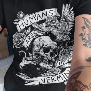 May include: Black t-shirt with a graphic design featuring a skull, roses, a bird, and the text "HUMANS ARE THE VERMIN". The design is in black and white.