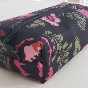 May include: A black zippered pouch with a floral print featuring pink, red, and green flowers. The pouch is made of a soft, durable fabric.