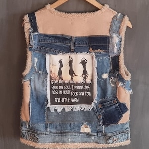 Op de afbeelding: Een patchwork denim vest met een beige imitatiebont voering. De achterkant heeft een rechthoekige patch met drie dansende silhouetten en de tekst "Give me the beat dogs and free my soul. I wanna get lost in your rock and roll and drift away."