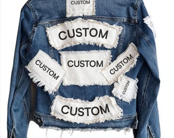 May include: A blue denim jacket with several white patches bearing the word "CUSTOM" in bold, black lettering. The jacket features a traditional collar, button fastenings, and distressed detailing.