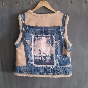 Op de afbeelding: Een spijkerbroekvest met een voering en accenten van beige imitatiebont. Het vest heeft een patch met de tekst "Give me the beat boys and free my soul, I wanna get lost in your rock and roll and drift away."