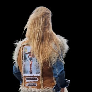 May include: A denim and brown suede vest with a faux fur collar. The back of the vest features a patch with an image of a person dancing in the rain, with the text "Dance with the rain" and "sing with the wind".