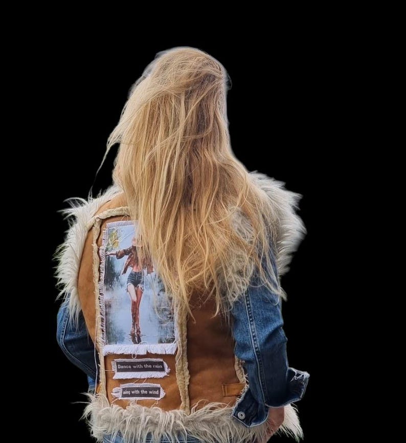 May include: A denim and brown suede vest with a faux fur collar. The back of the vest features a patch with an image of a person dancing in the rain, with the text "Dance with the rain" and "sing with the wind".