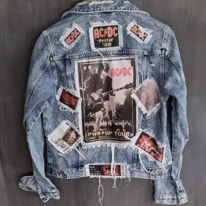 May include: A light blue denim jacket with several patches, including a large AC/DC patch with a concert image and the text "PWR UP TOUR".