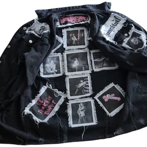 Op de afbeelding: Zwarte spijkerjas met meerdere patches en fotovierkanten. Patches met de tekst "YUNGBLUD" en "WE F**KIN HAPPY". De jas heeft een knoopsluiting en distressed details, die een punkrock-esthetiek laten zien.