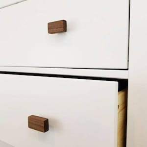 May include: White dresser with two drawers and wooden knobs. The bottom drawer is open, revealing a wooden interior.