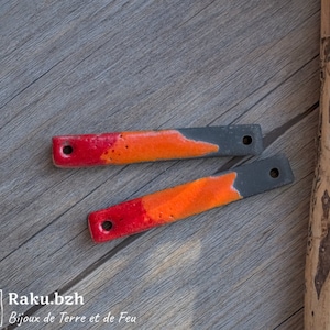 Peut inclure: Deux petites pièces rectangulaires en céramique colorées avec des trous à chaque extrémité. Les pièces sont peintes dans des tons de rouge, orange et noir. Les pièces sont sur une surface en bois.