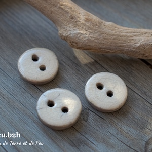 Peut inclure: Trois boutons en céramique blanche avec deux trous chacun. Les boutons sont sur une surface en bois.