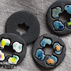 Peut inclure: Quatre ornements ronds en céramique noire avec un motif floral. Chaque ornement a un glaçage de couleur différente, y compris le bleu, le vert, le jaune et le violet. Les ornements ont un trou au centre en forme d'étoile.