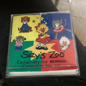 May include: A clear plastic case featuring the text "Suzy's Zoo" and various cartoon animal characters. The case has a colorful design with a yellow, green, blue, and red background. The text "Exclusively for BERNINA Collection No. 101" is also visible.