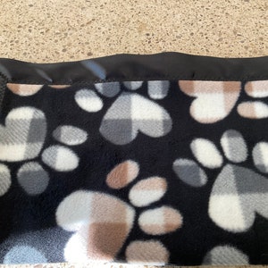 May include: Black fleece blanket with a paw print pattern in shades of gray, white, and brown. The blanket has a black satin border.