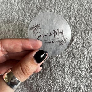 May include: Clear round sticker with black floral design and the text "Sophie & Mark 17.04.2024"