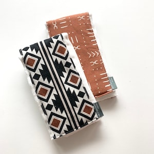 May include: Two cotton burp cloths with geometric patterns. One cloth is brown with white geometric designs. The other cloth is black and white with brown geometric designs. Both cloths have a white border and a white label that says "Lucy Locket Designs".