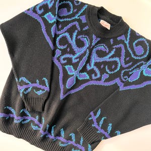May include: Black sweater with a blue and purple patterned design. The pattern is a repeating design of leaves and swirls.
