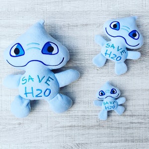Könnte beinhalten: Drei blaue Plüschtiere in Form einer Comicfigur mit großen Augen. Die Spielzeuge haben den Text "SAVE H2O" aufgestickt.
