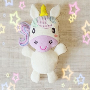 May include: A white plush unicorn toy with a yellow horn, embroidered details, and a pink muzzle. The unicorn has a colorful mane and a smiling face. The toy is approximately 10 inches tall.