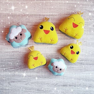May include: A collection of handmade plush toys, including yellow chicks with red beaks and crowns, and blue sheep with white wool. The toys are arranged on a light wood-grain surface, creating a cheerful and whimsical scene.
