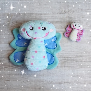 Könnte beinhalten: Ein blaues Plüsch-Schmetterlings-Spielzeug mit einem lächelnden Gesicht und rosa Punkten. Der Schmetterling hat große blaue Flügel mit weißen Sternen. Ein kleineres rosa Schmetterlings-Spielzeug mit einem gelben Körper und weißen Flügeln ist ebenfalls abgebildet.