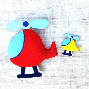 May include: Two plush toy helicopters. The larger helicopter is red with blue accents and a white propeller. The smaller helicopter is yellow with blue accents and a white propeller.