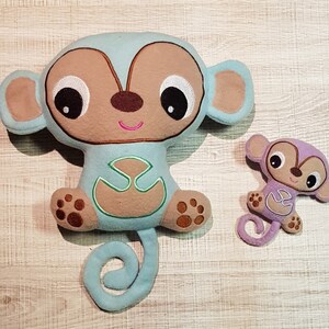 May include: Two plush monkey toys, one large and one small. The larger monkey is light blue with brown ears and a brown face. The smaller monkey is purple with brown ears and a brown face. Both monkeys have embroidered eyes and a smiling mouth.