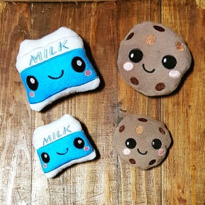 May include: Three plush toys: a brown cookie with a smiling face, and two blue milk cartons with smiling faces and the word "MILK" on them.