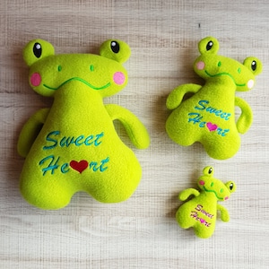 May include: Three plush green frog toys with embroidered hearts and the text "Sweet Heart".