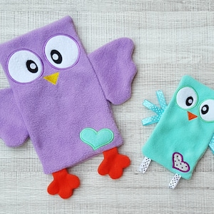 May include: Two plush owl toys, one purple with a green heart and one teal with a white heart. Both owls have embroidered eyes and beaks.