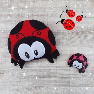 May include: Two plush ladybug toys. The larger ladybug is red with black spots and white eyes. The smaller ladybug is pink with black spots and white eyes.