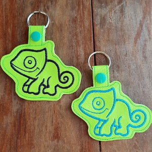 May include: Two green leather keychains with black and blue embroidered chameleon designs. The keychains have a silver ring and a turquoise button.