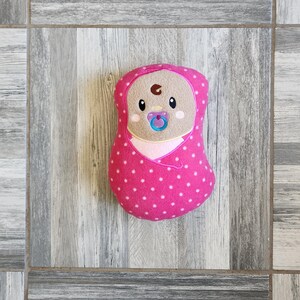 May include: A pink and white polka dot baby doll with a brown embroidered face and a blue pacifier.