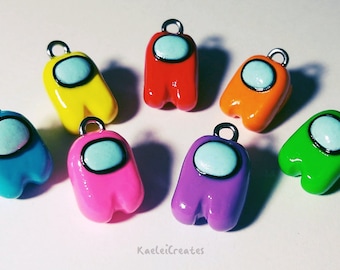 May include: Seven colorful Among Us character charms made of polymer clay. The charms are in the colors red, yellow, orange, blue, pink, purple, and green.