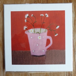May include: A square art print featuring a painting of a light pink pitcher with white polka dots containing a bouquet of white daisies. The pitcher sits on a brown surface against a solid red background. The artist signature is in the corner.