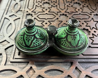 May include: Two small green ceramic bowls with black and white designs, sitting on a wooden tray with intricate carvings.