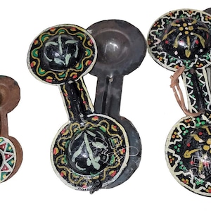 May include: Set of six castanets, a traditional Spanish percussion instrument. The castanets are made of wood and painted with intricate designs in black, red, green, and yellow. Each castanet has a small, round, black center with a decorative design.