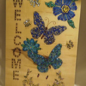 Welcome sign wood burned flowers butterflies and bees painted in blue  teal and green embellished with colored crystals