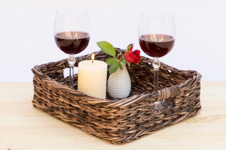 May include: A wicker tray with two glasses of red wine, a lit candle, and a small vase with a single red rose.