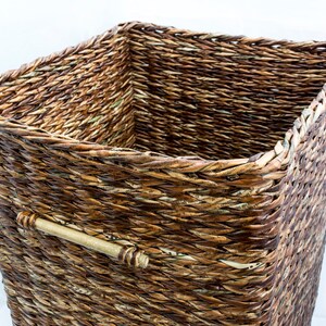 May include: A woven storage basket made of natural materials, with a brown and tan color scheme. The basket has a rectangular shape and a handle on the side.