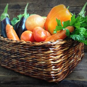 May include: A wicker basket filled with fresh produce, including carrots, onions, eggplant, tomatoes, and a bright orange bell pepper.
