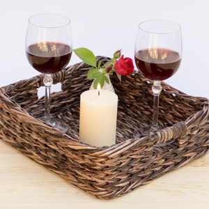 May include: A wicker tray with two glasses of red wine, a lit candle, and a single red rose in a small white vase.