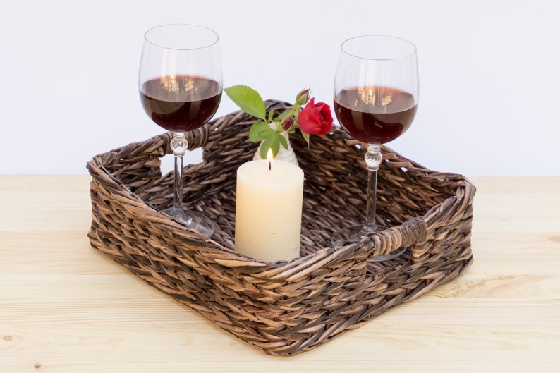 May include: A wicker tray with two glasses of red wine, a lit candle, and a single red rose in a small white vase.