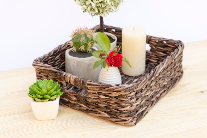 May include: A brown wicker tray with a white candle, a small potted succulent, a small potted rose, and a small potted topiary.