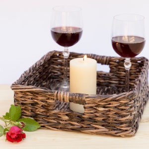 May include: A wicker tray with two glasses of red wine and a lit candle. A single red rose with green leaves is on the table next to the tray.