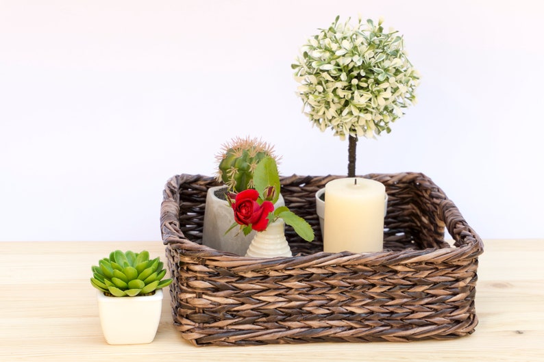 May include: A brown wicker tray with a white candle, a small potted succulent, a small potted cactus, and a small potted red rose.