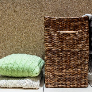 May include: A brown wicker storage basket with a handle, a green knitted throw pillow, and a white knitted throw pillow on a tiled floor.