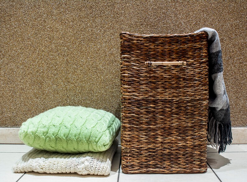 May include: A brown wicker storage basket with a handle, a green knitted throw pillow, and a white knitted throw pillow on a tiled floor.
