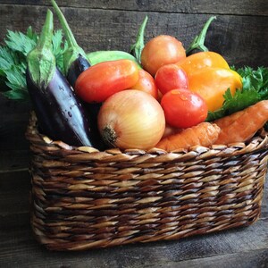 May include: A wicker basket filled with fresh produce, including eggplant, tomatoes, onions, carrots, and a yellow bell pepper.