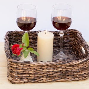 May include: A wicker tray with two glasses of red wine, a lit candle, and a single red rose in a small white vase.