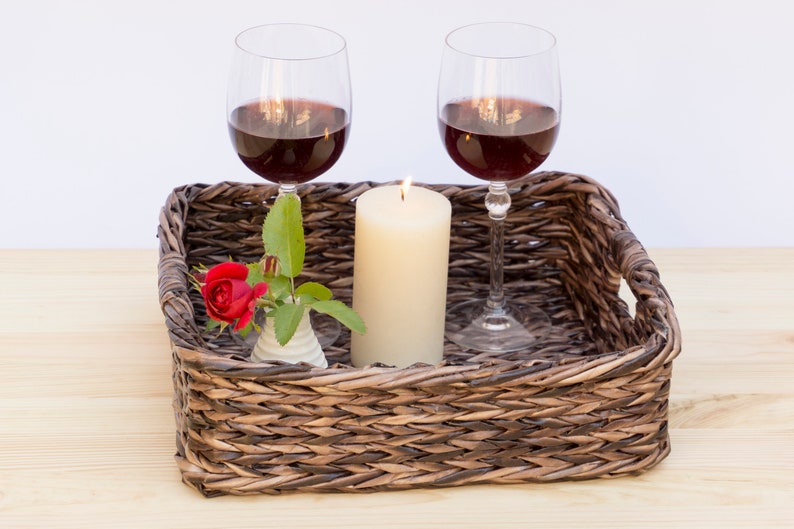 May include: A wicker tray with two glasses of red wine, a lit candle, and a single red rose in a small white vase.