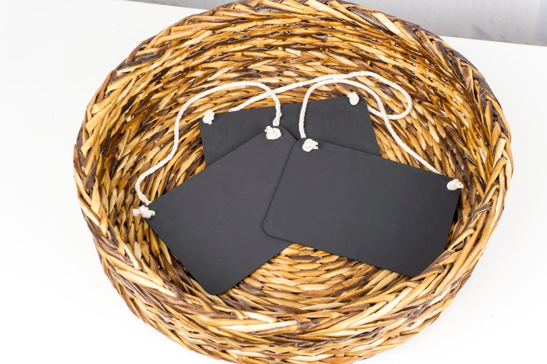 May include: Three black chalkboard tags with white string attached, sitting in a woven wicker basket.