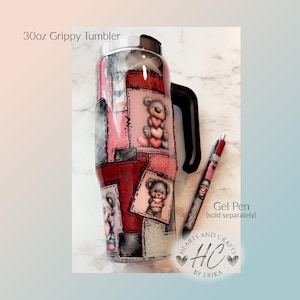 May include: A 30oz Grippy Tumbler with a black handle and a matching gel pen. The tumbler features a patchwork design with teddy bear illustrations holding hearts. The gel pen is red and silver. The text "Hearts and Crafts by Erika" is also visible.